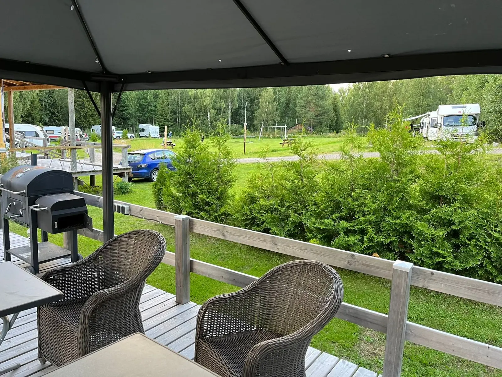 Terras met rieten stoelen en barbecue, met uitzicht over de camping